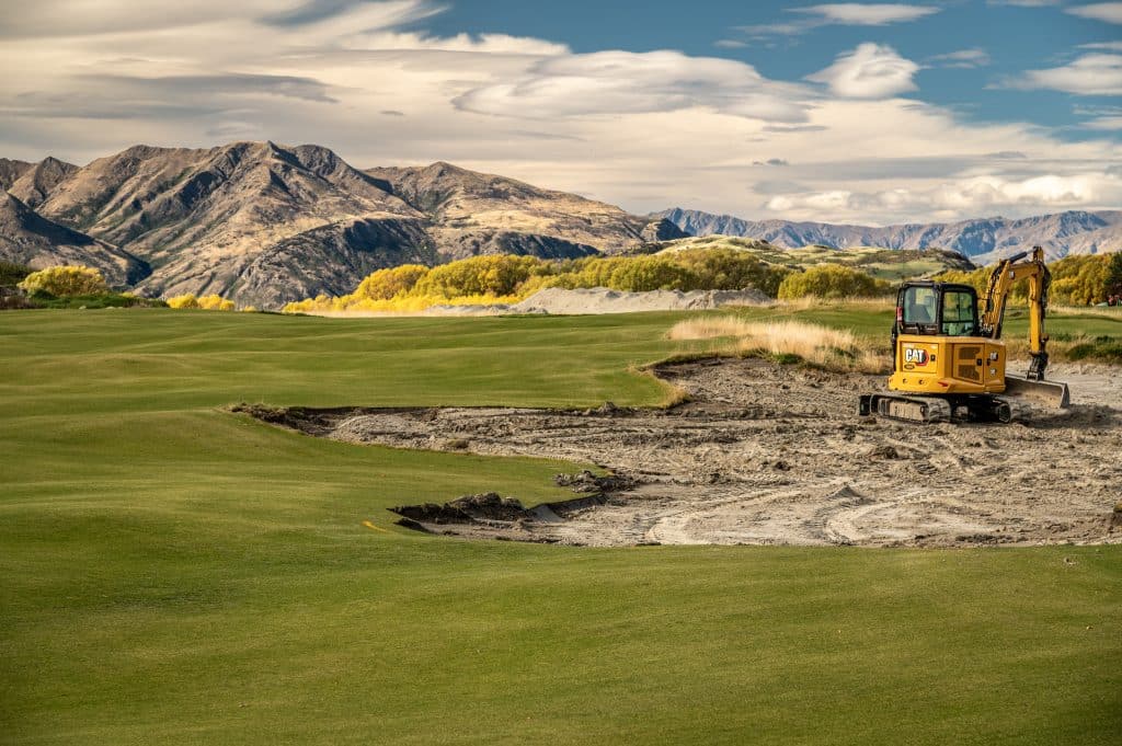 Golf course construction – shaping bunker with excavator beside finished green Wanaka