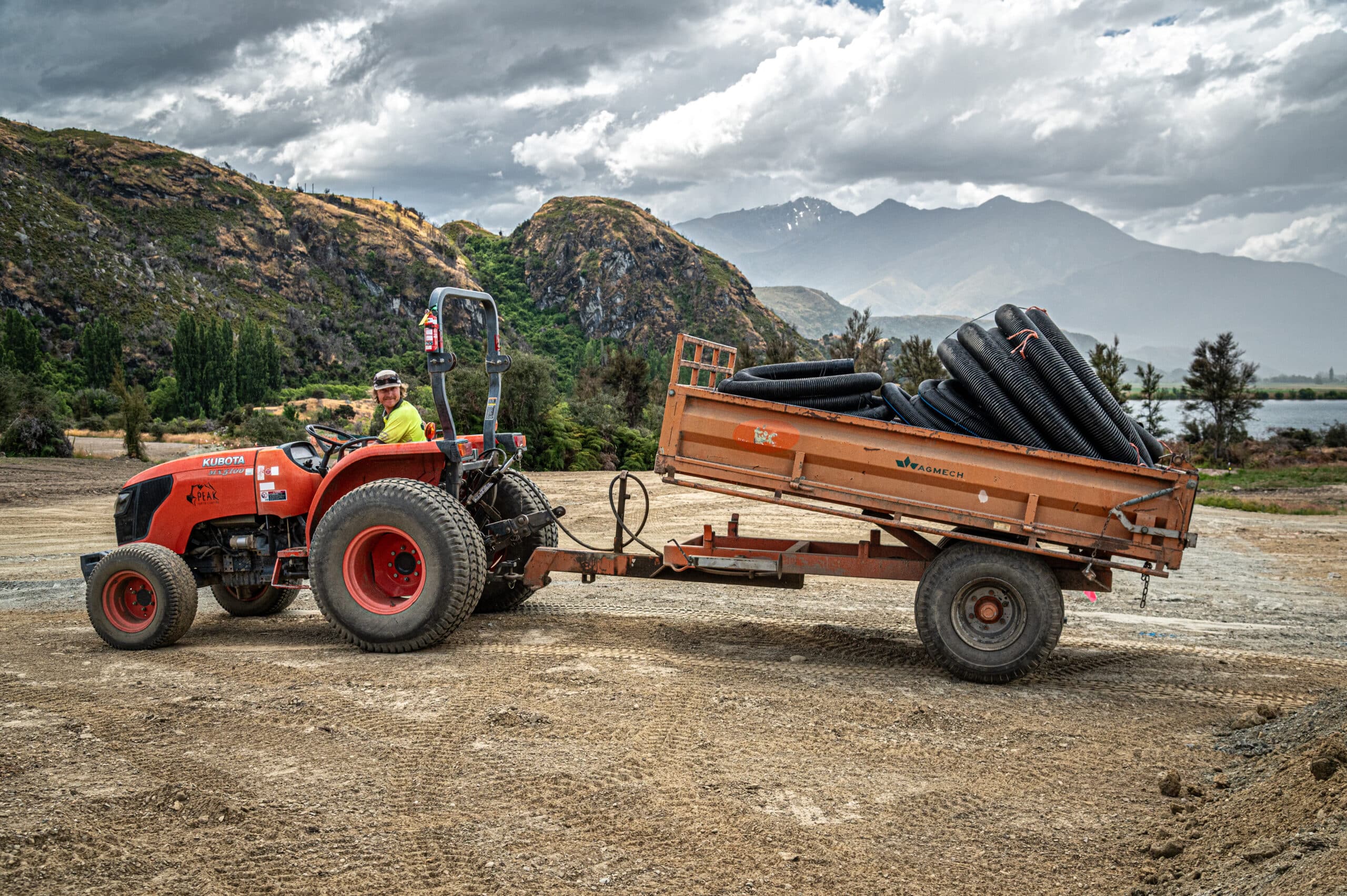 Kubota MX5100DT compact tractor with tipping trailer transporting drainage material on an earthworks site — Peak Earth Shaping